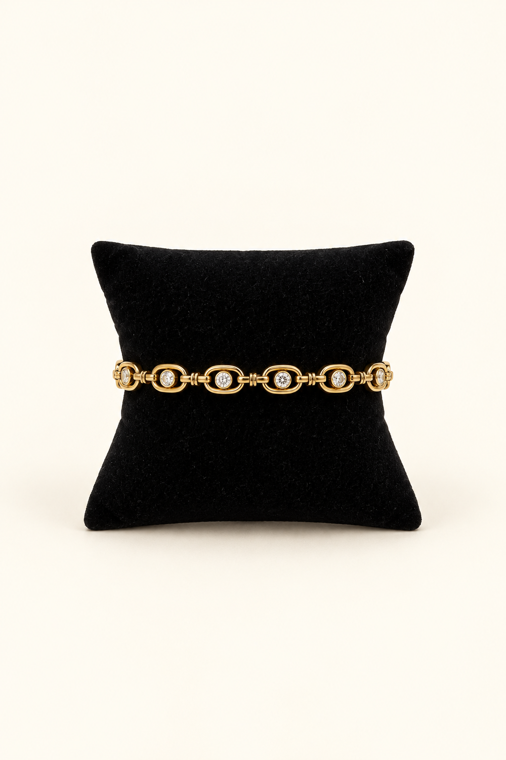 Gold link bracelet featuring round crystal stones rimmed in smooth polished gold, displayed on a black velvet jewelry pillow against a warm cream background.