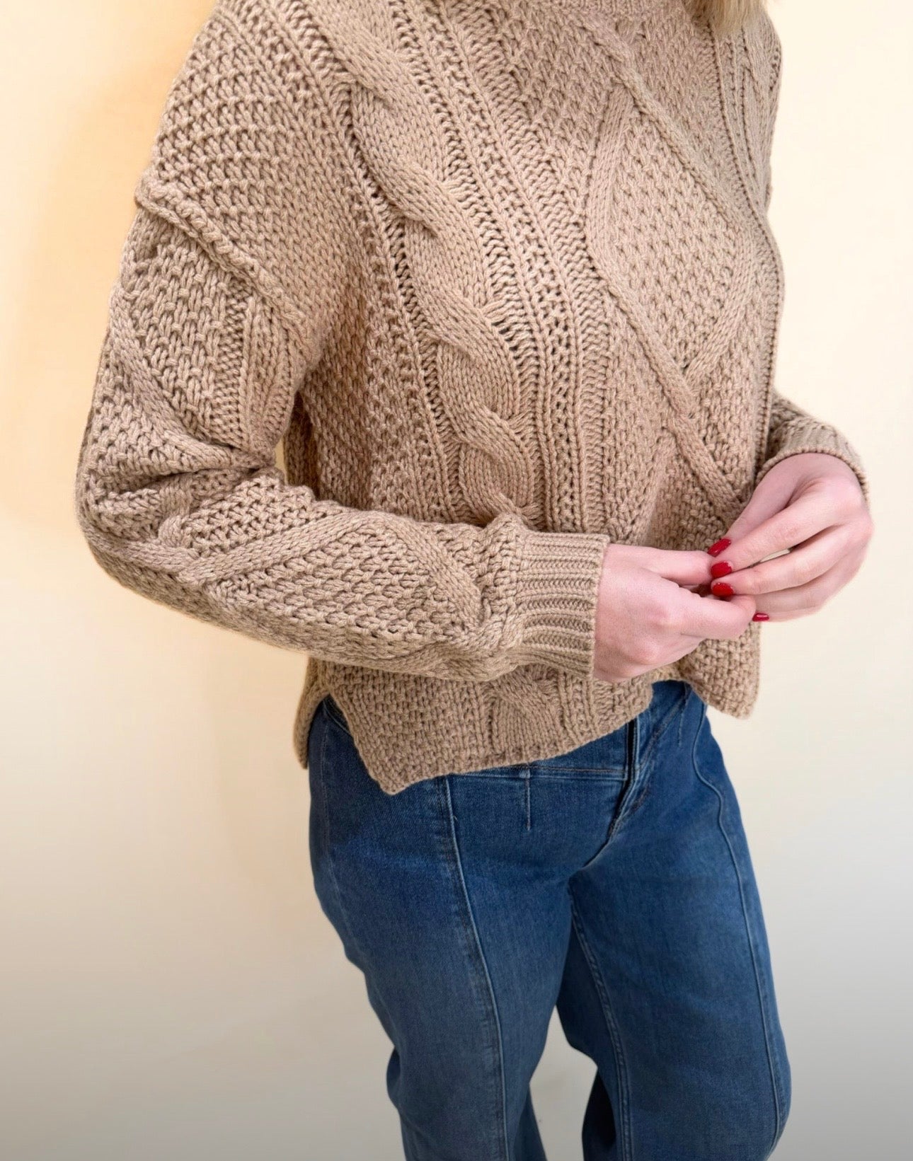 Close-up detail of tan cable knit sweater featuring textured stitching and braided pattern, styled with blue denim jeans.