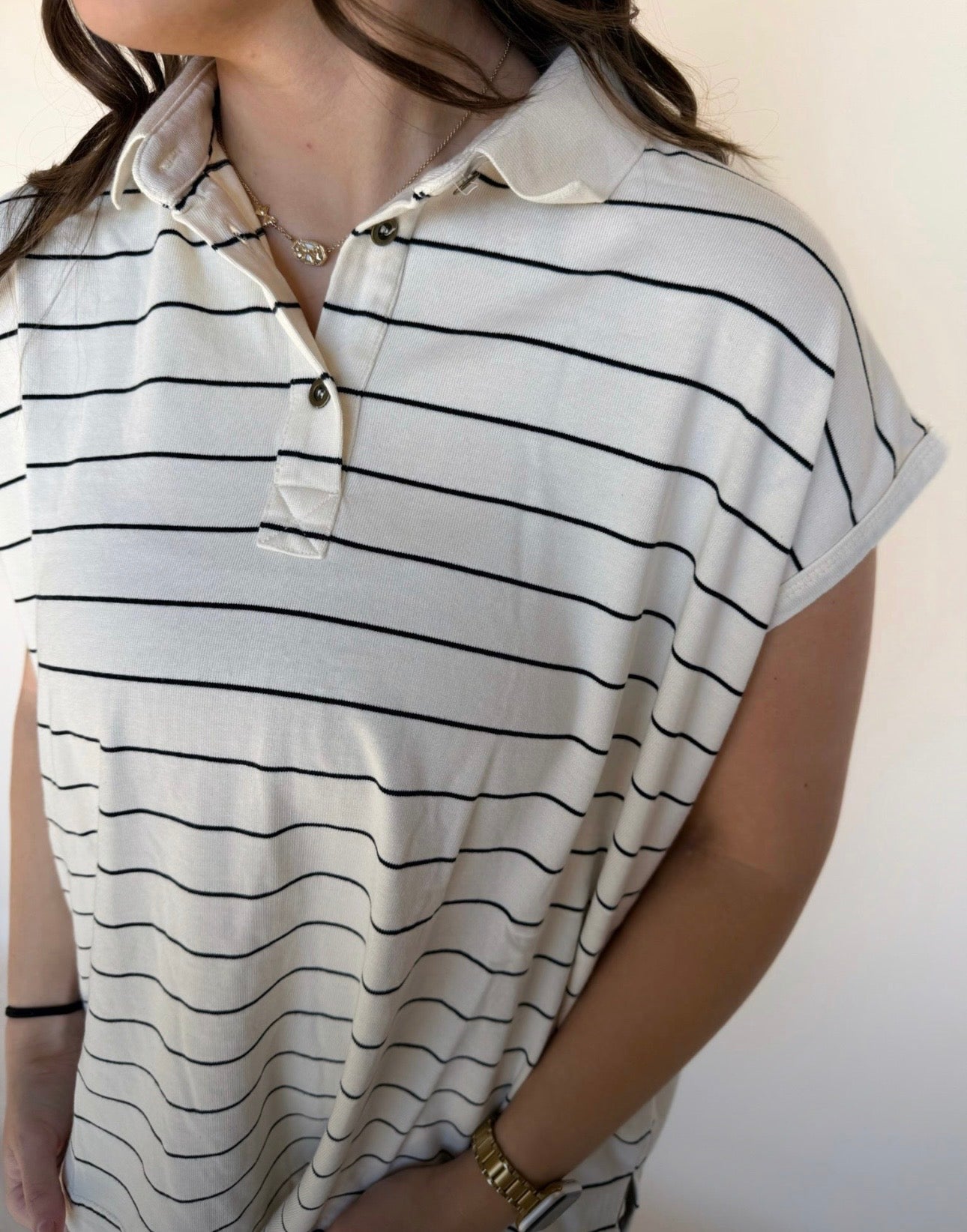 Close-up detail of a cream collared top with thin black stripes, showing the button placket and rolled sleeves. 
