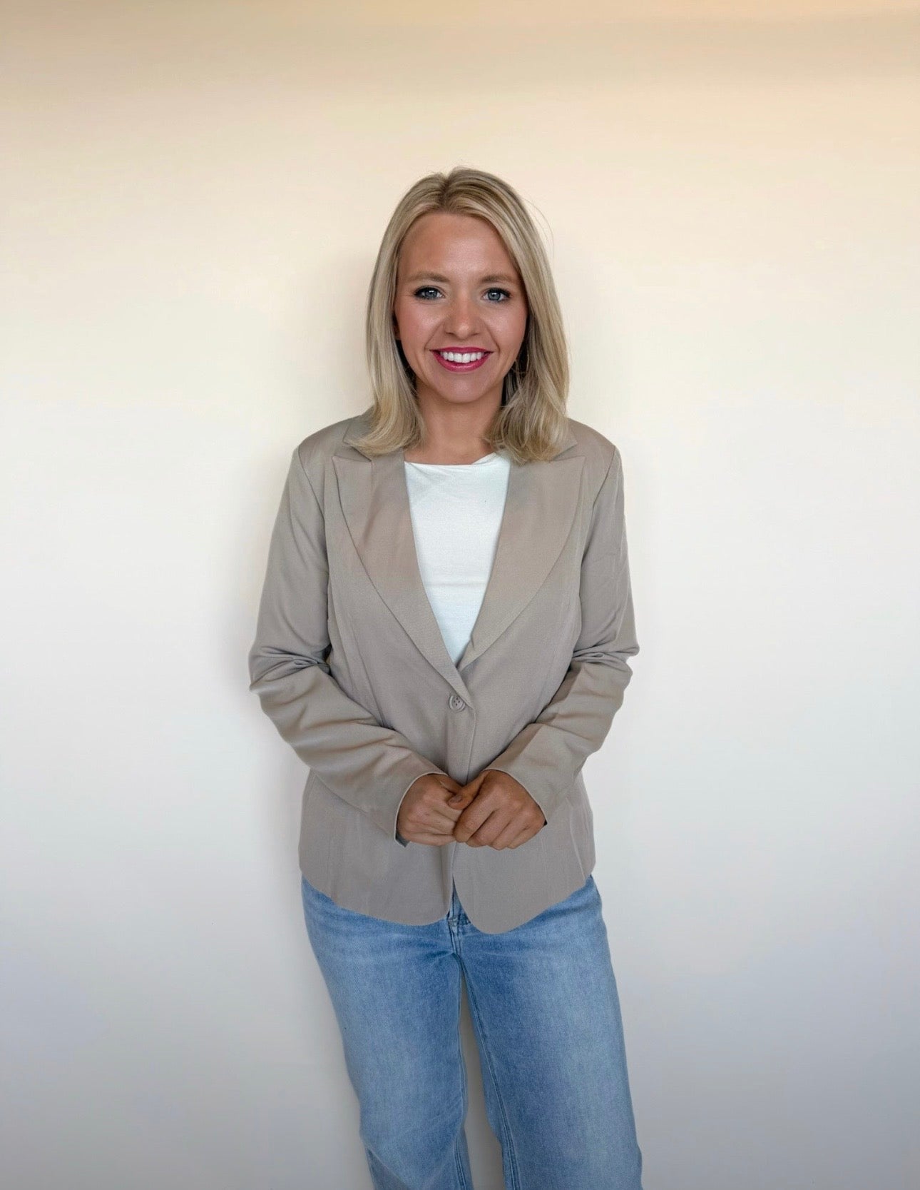 Woman wearing a beige blazer and blue jeans against a plain background