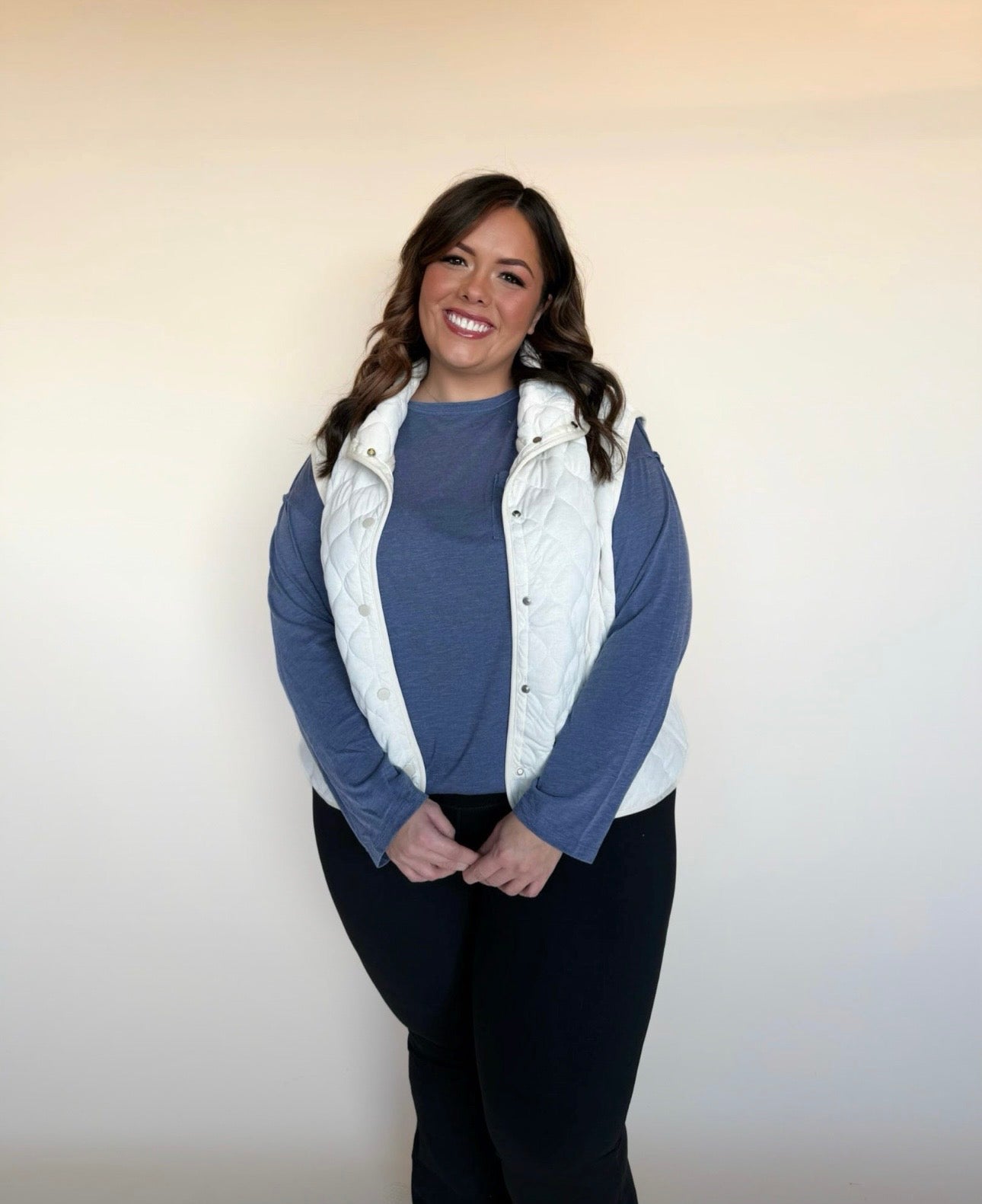 Woman wearing a blue sweater and white vest against a plain background
