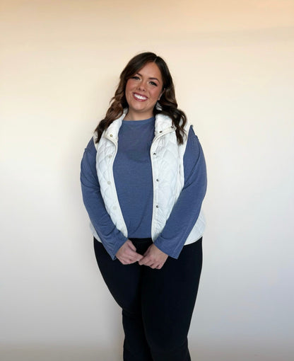Woman wearing a blue sweater and white vest against a plain background