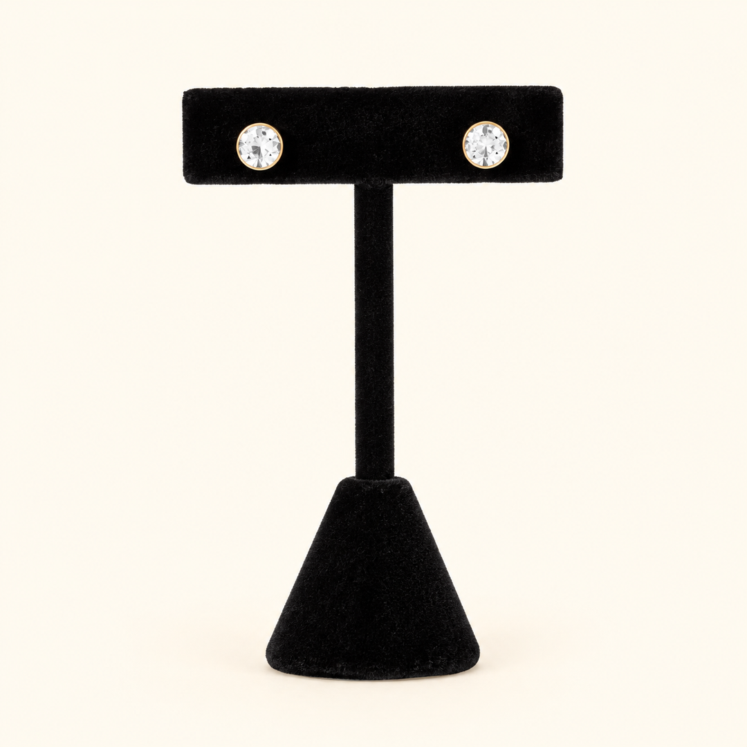 6mm round clear crystal stud earrings with gold-tone settings displayed on a black velvet T-bar jewelry stand against a cream background.