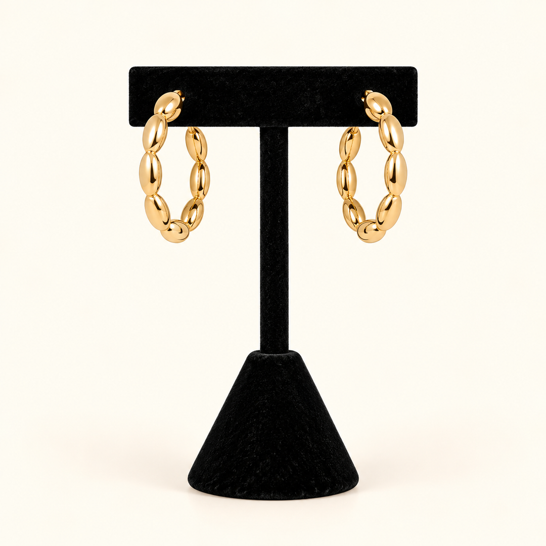 1-inch gold-tone oval bead hoop earrings with a high-shine finish displayed on a black velvet T-bar jewelry stand against a cream background.