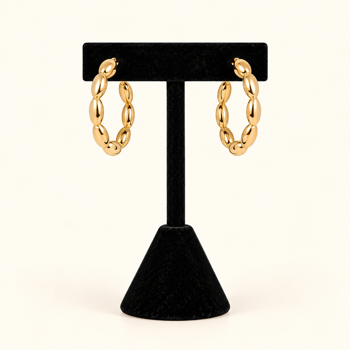 1-inch gold-tone oval bead hoop earrings with a high-shine finish displayed on a black velvet T-bar jewelry stand against a cream background.