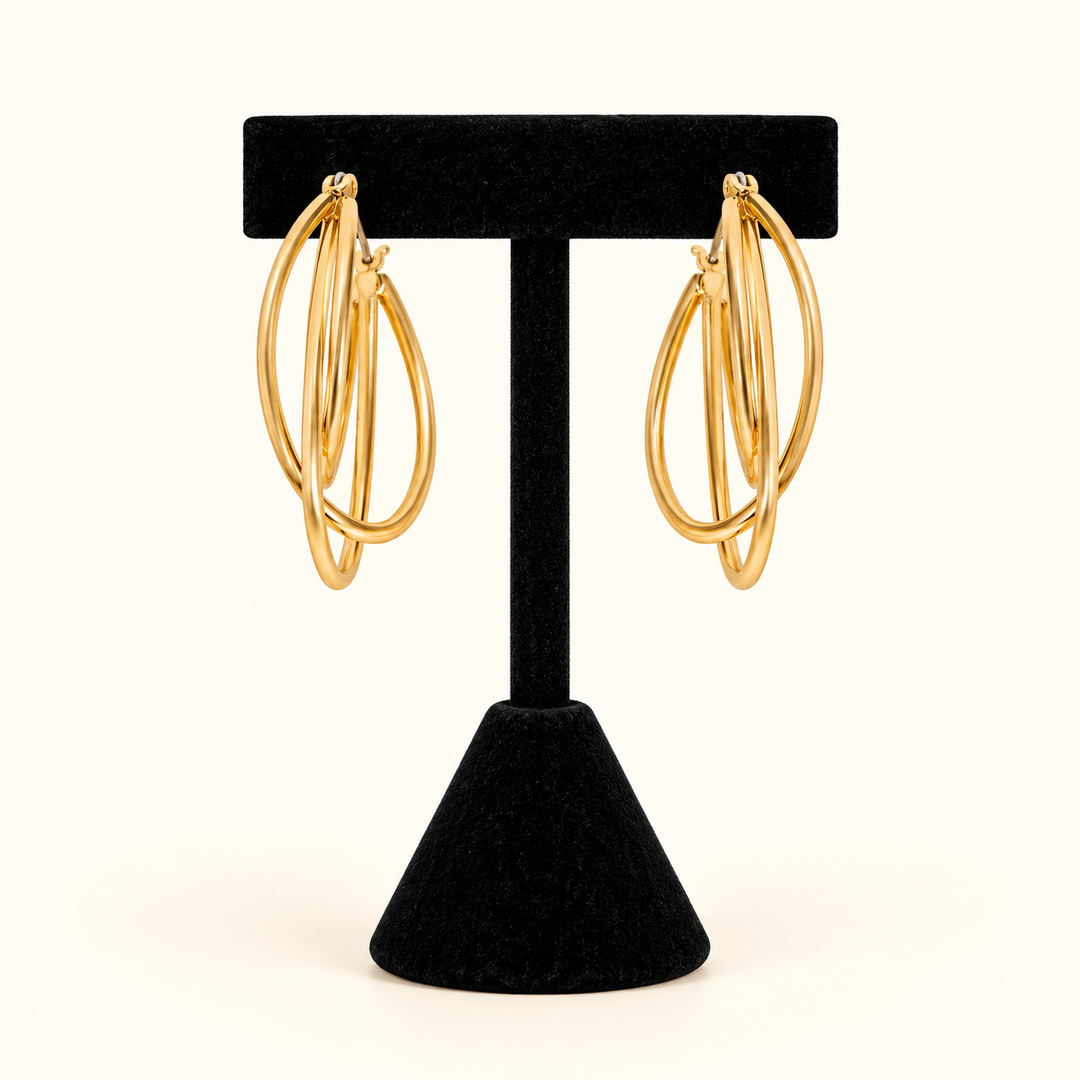 1.5-inch gold-tone layered triple hoop earrings with an overlapping oval design displayed on a black velvet T-bar jewelry stand against a cream background.