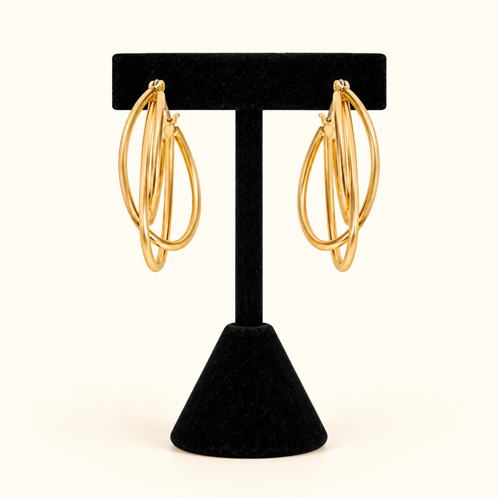 1.5-inch gold-tone layered triple hoop earrings with an overlapping oval design displayed on a black velvet T-bar jewelry stand against a cream background.