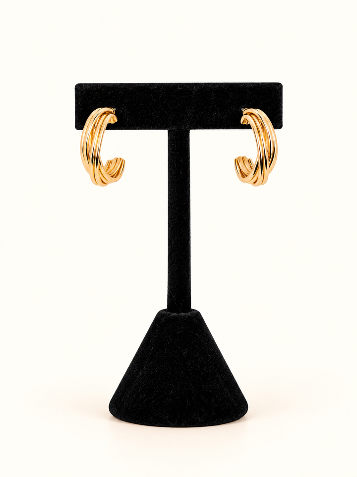 Chunky 0.75-inch gold-tone multi-band hoop earrings with a polished, layered C-shaped silhouette displayed on a black velvet T-bar jewelry stand against a cream background.