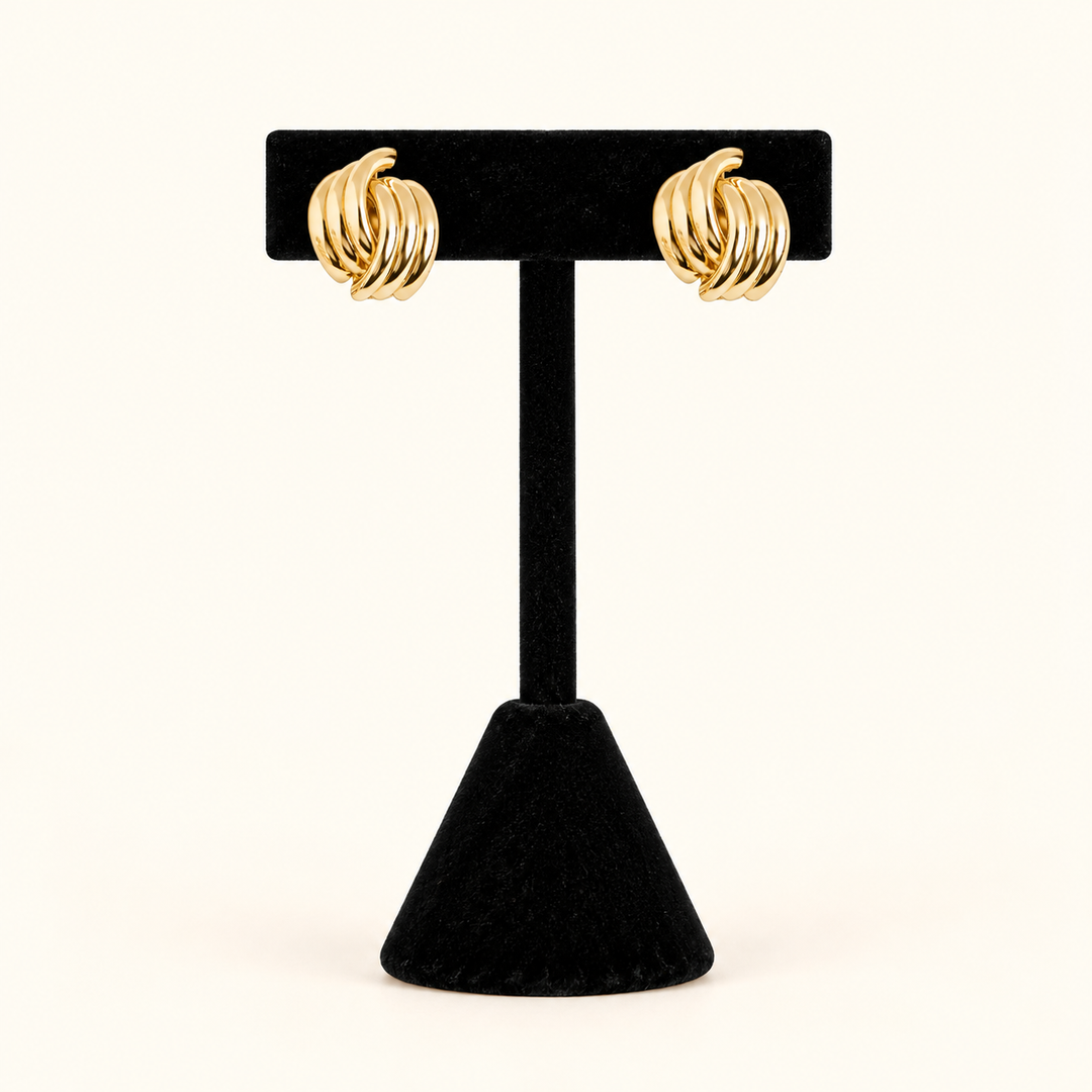0.5-inch gold-tone knot hoop earrings with layered, high-shine metal bands displayed on a black velvet T-bar jewelry stand against a cream background.