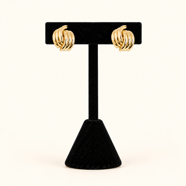 0.5-inch gold-tone knot hoop earrings with layered, high-shine metal bands displayed on a black velvet T-bar jewelry stand against a cream background.