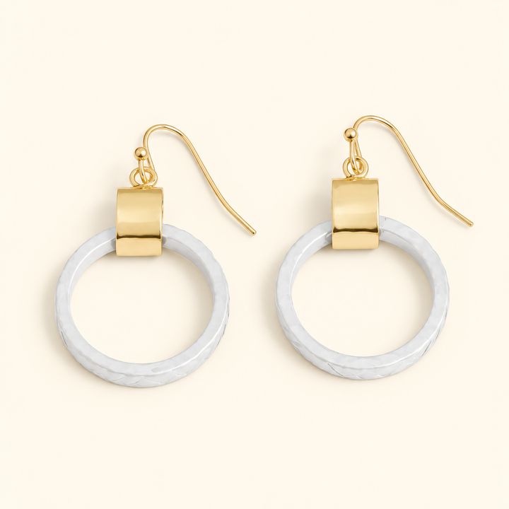 White textured circle drop earrings with gold-tone accents and fishhook closures, featuring a 2-inch dangle design on a cream background.