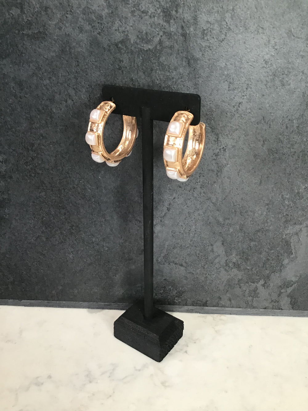 Pearl and gold hoop earrings on a black stand against a gray background
