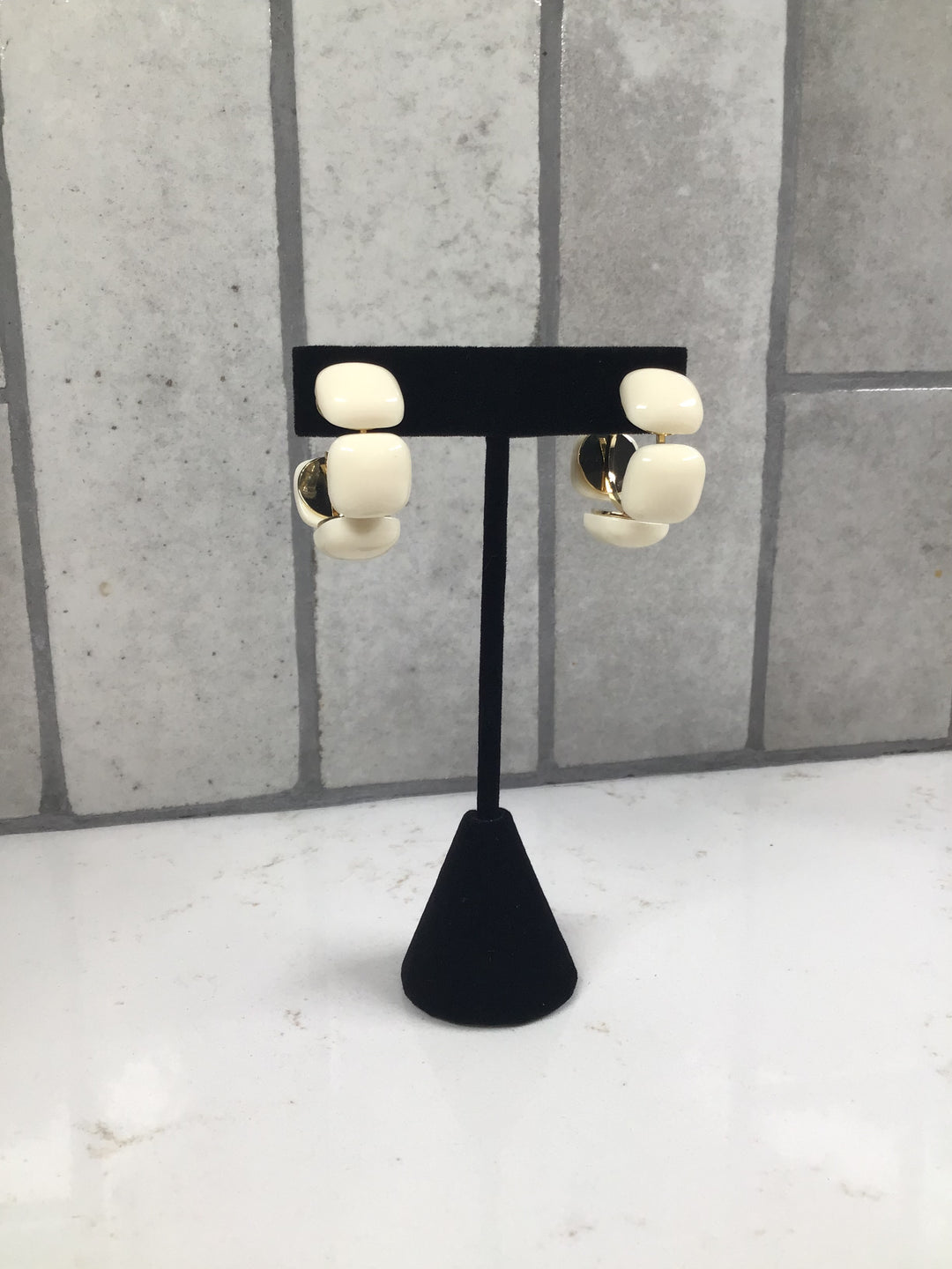 Cream linked acrylic square hoop earrings displayed on a black jewelry stand with gold accents.