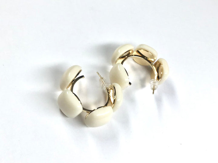 Close-up of cream linked acrylic square hoop earrings with gold accents on a white background.