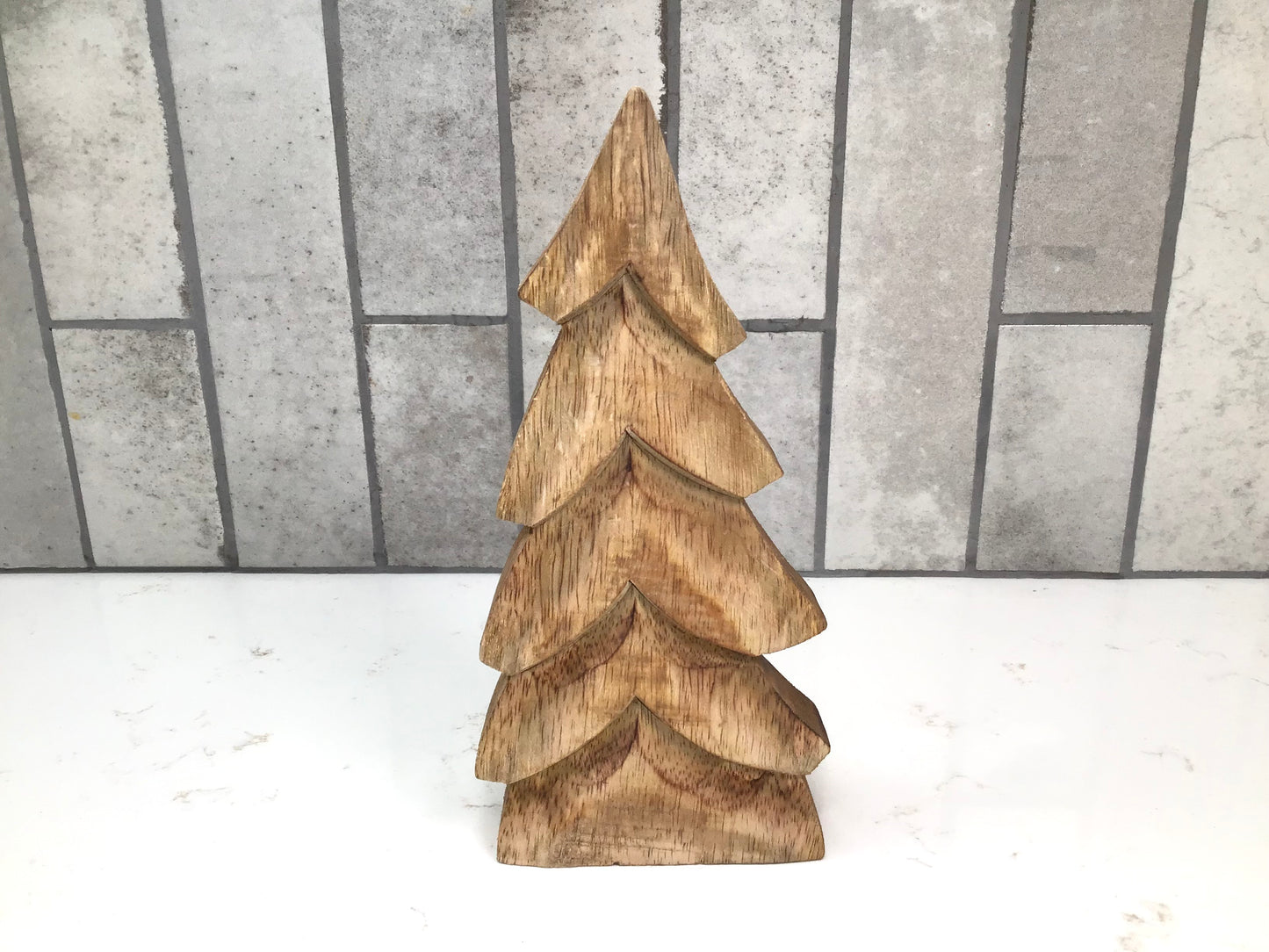 Wooden Christmas tree decoration on a white surface with a gray tiled background