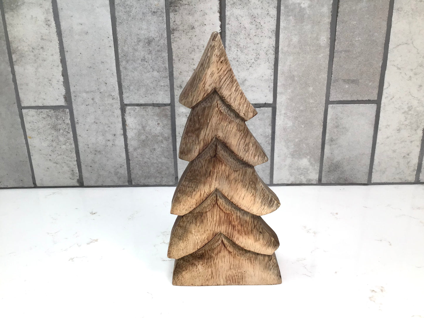 Wooden Christmas tree decoration on a white surface with a gray tiled background