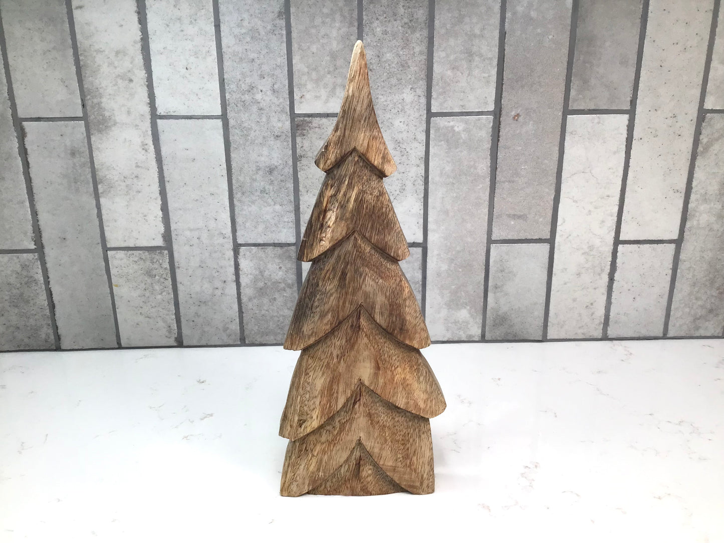 Wooden Christmas tree decoration on a white surface with a tiled wall background