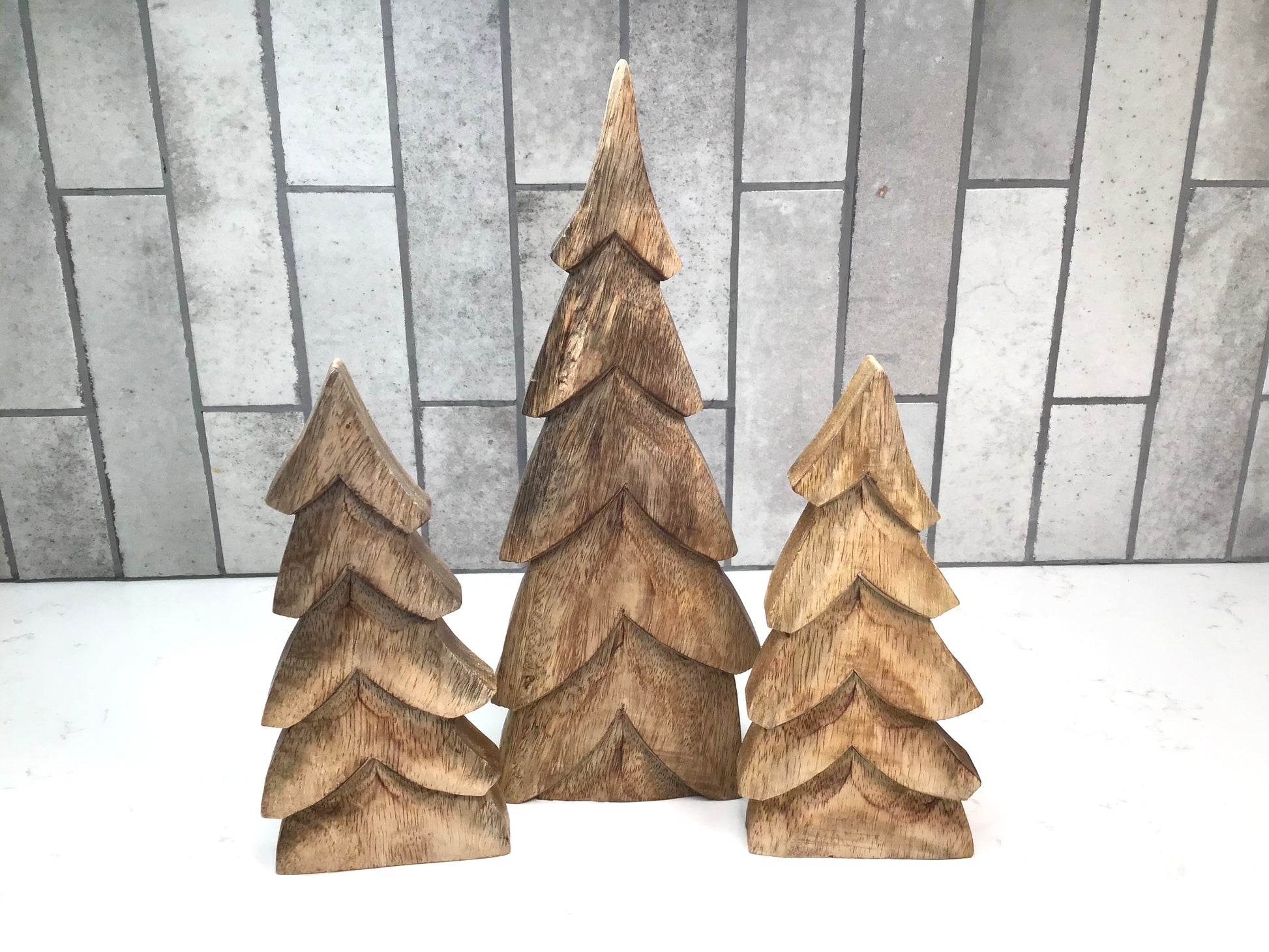 Three wooden Christmas trees on a white surface with a gray tiled background