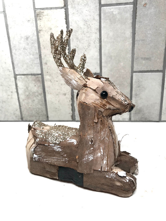 Decorative reindeer made from driftwood with glittery antlers on a white surface.