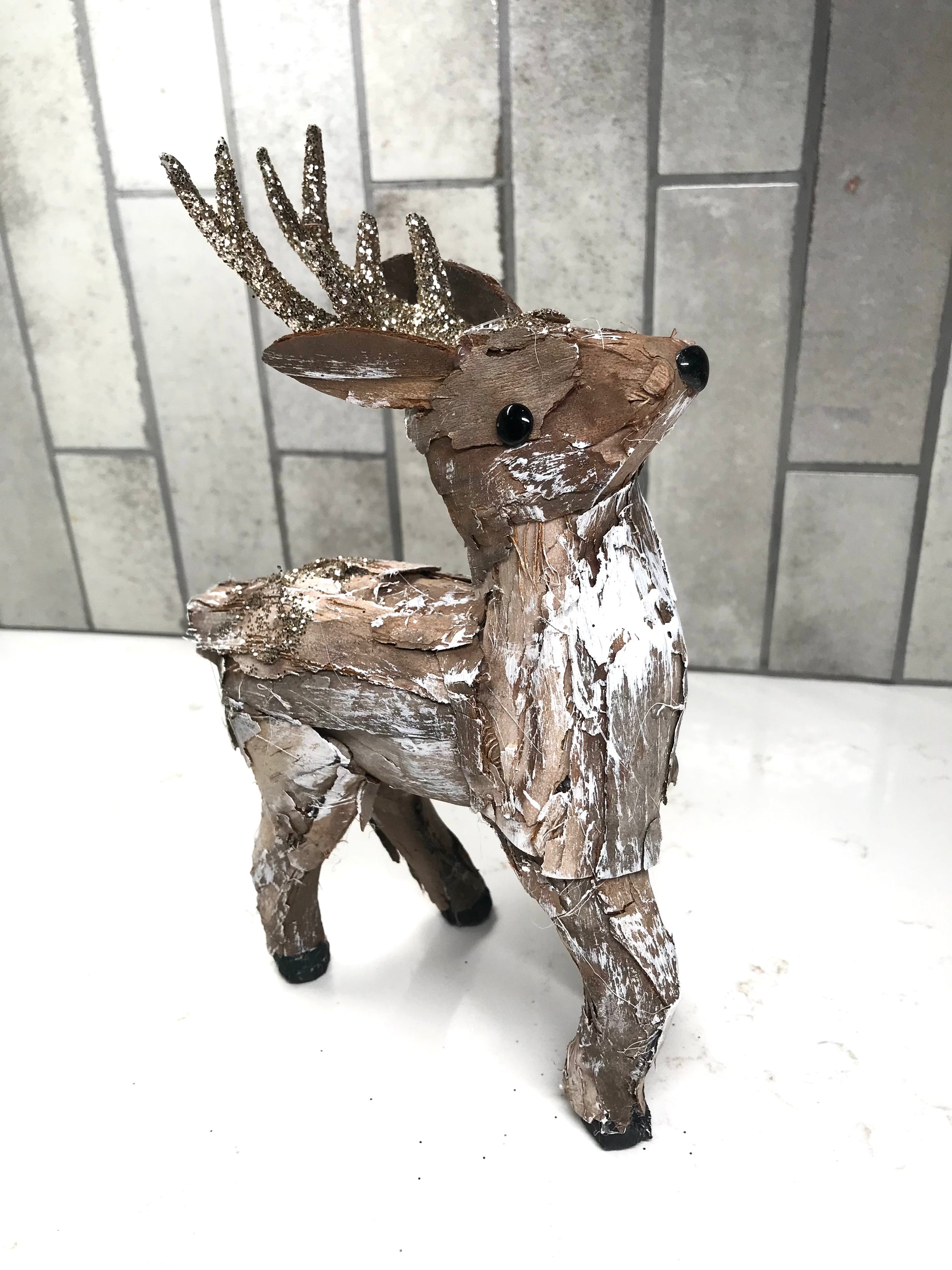 Decorative deer figure with metallic finish on a white surface and tiled wall background