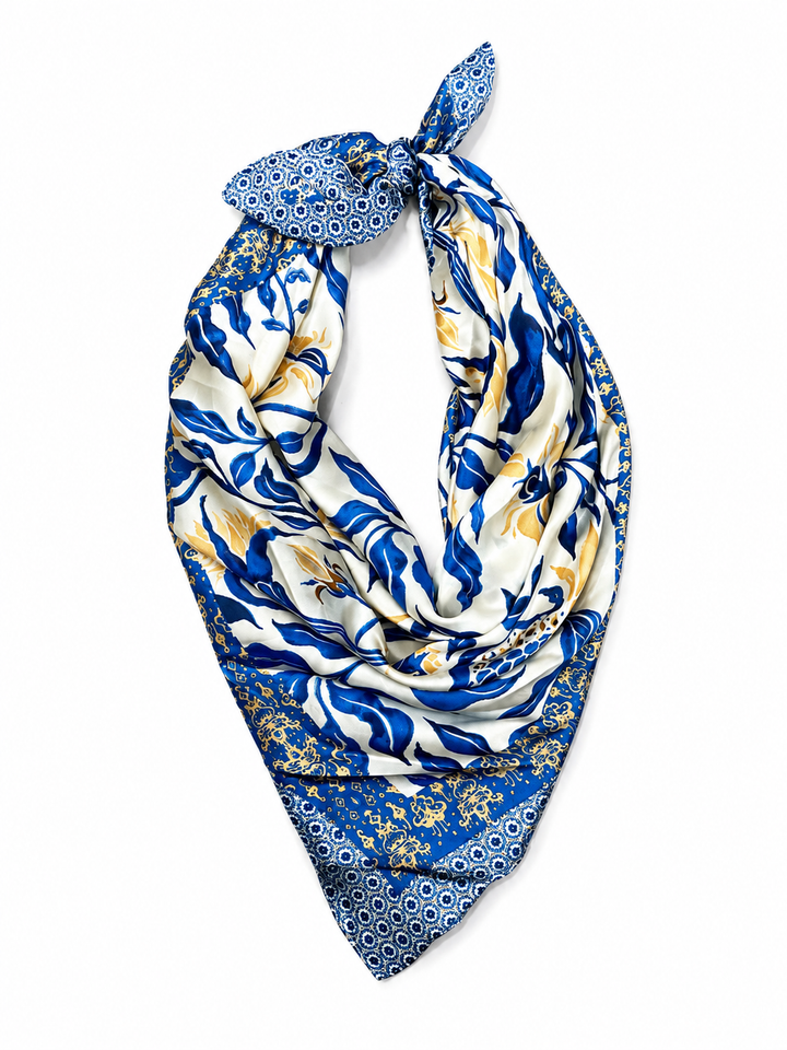 A square silk scarf with a blue, white, and nude botanical pattern, tied in a loop at the top and displayed against a solid white background.