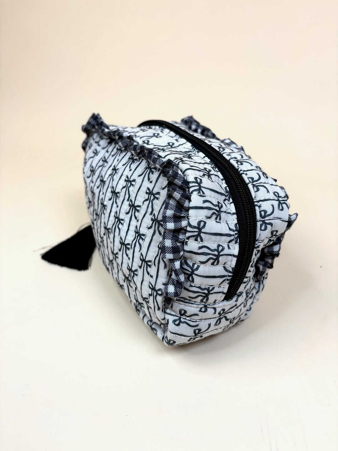 Side view of the Simply Southern Black Bow Quilted Cosmo Bag showcasing the quilted bow print, ruffle trim, zip-top closure, and structured cosmetic bag silhouette on a cream studio background.