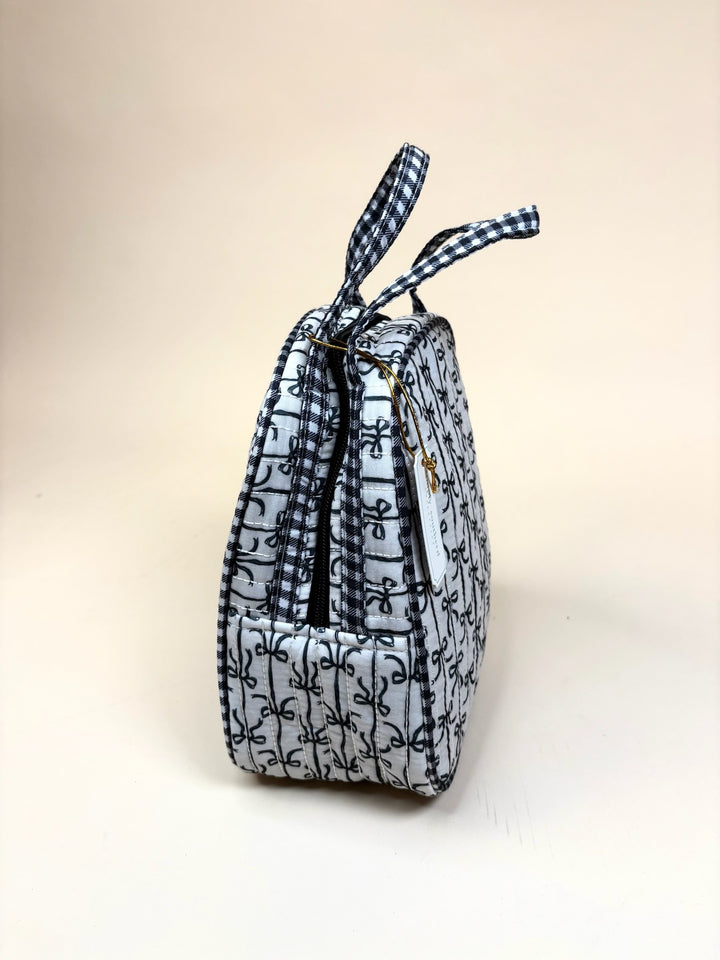 Side view of the Simply Southern Black Bow Quilted Lunch Bag showcasing its insulated profile, quilted bow print, dual handles, and zip-top closure on a cream studio background.