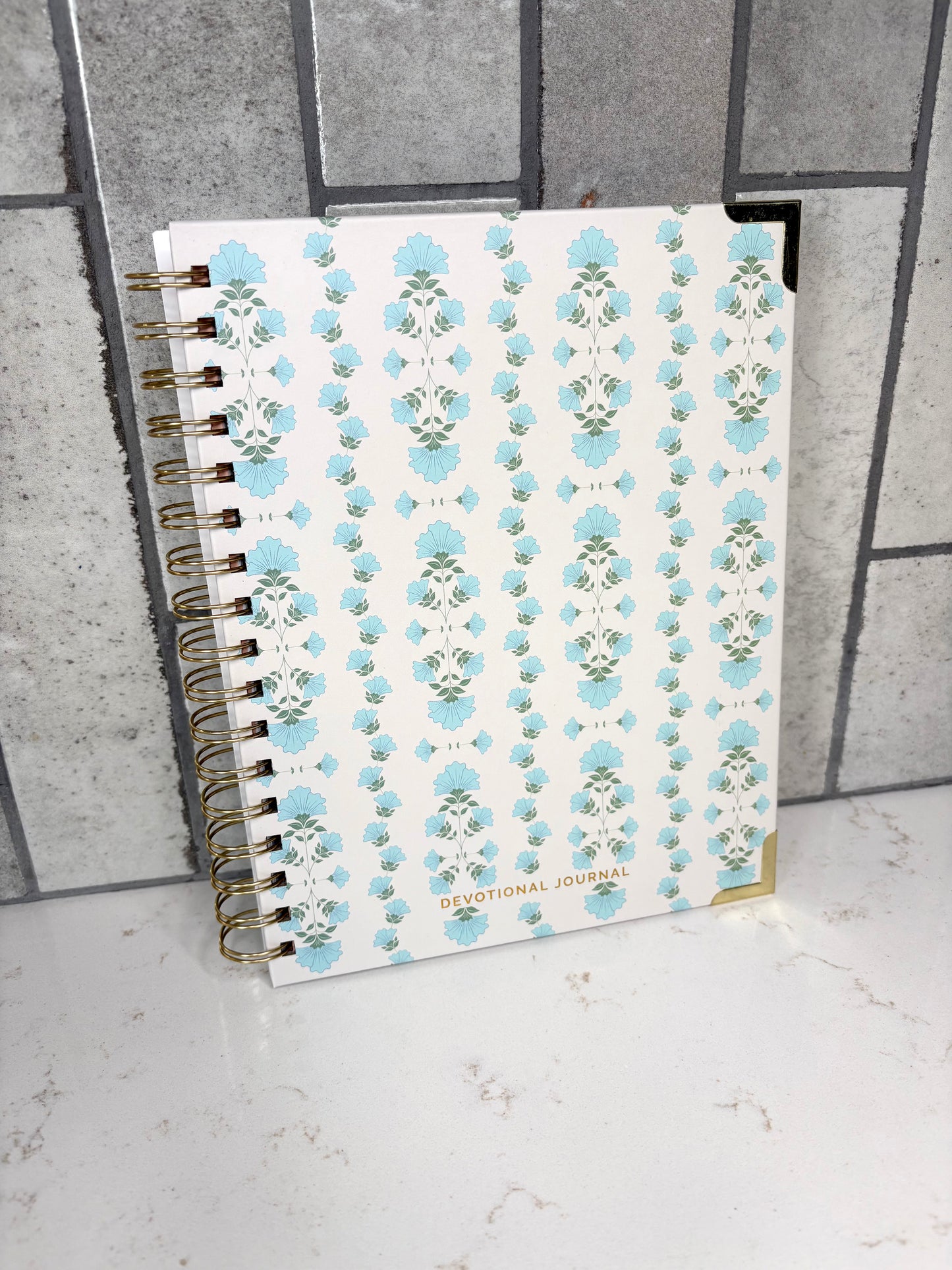 Blue floral Christian devotional journal with gold spiral binding, faith-based Bible study notebook for prayer, scripture reflection, and daily devotional writing.