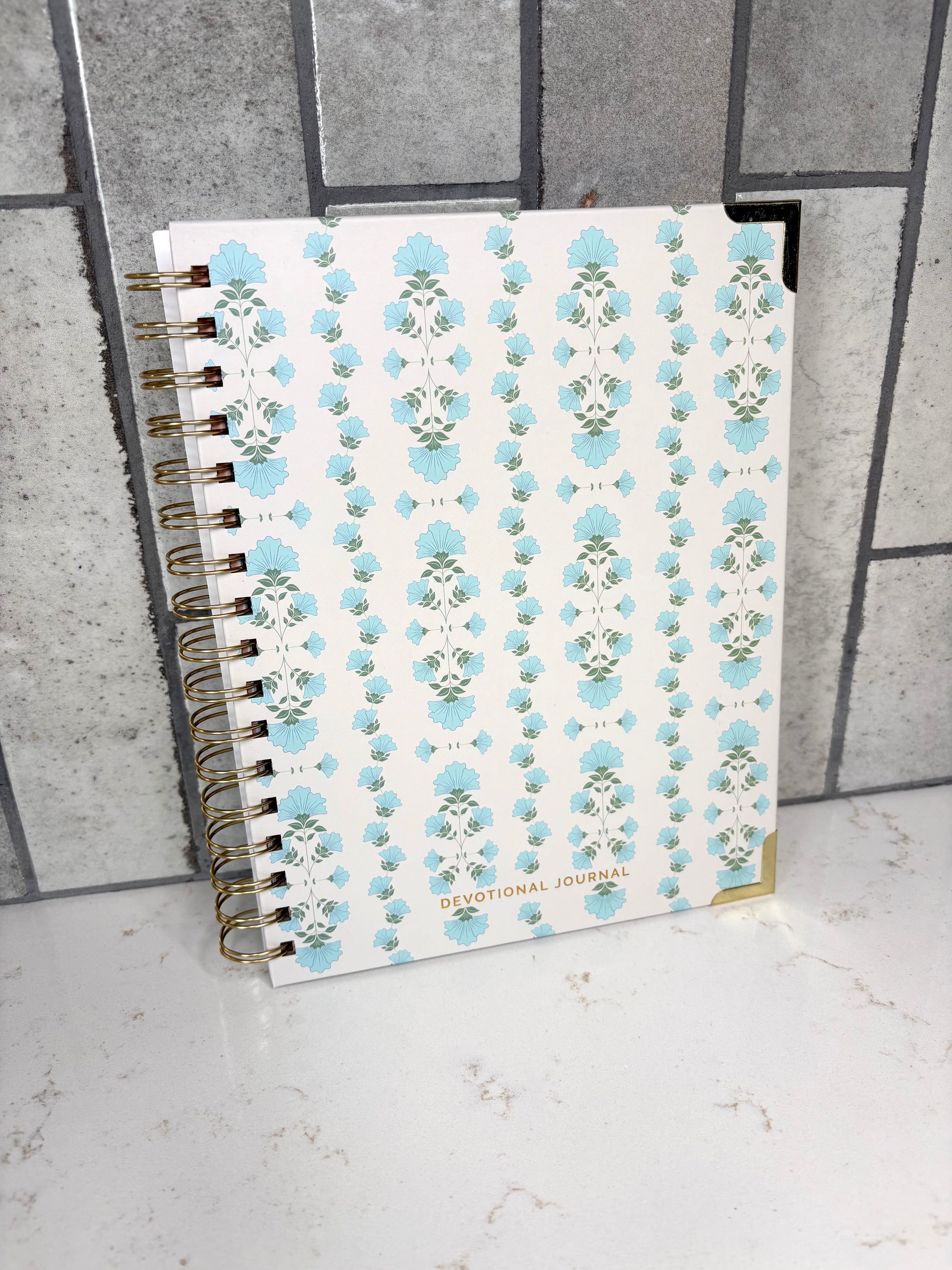 Blue floral Christian devotional journal with gold spiral binding, faith-based Bible study notebook for prayer, scripture reflection, and daily devotional writing.
