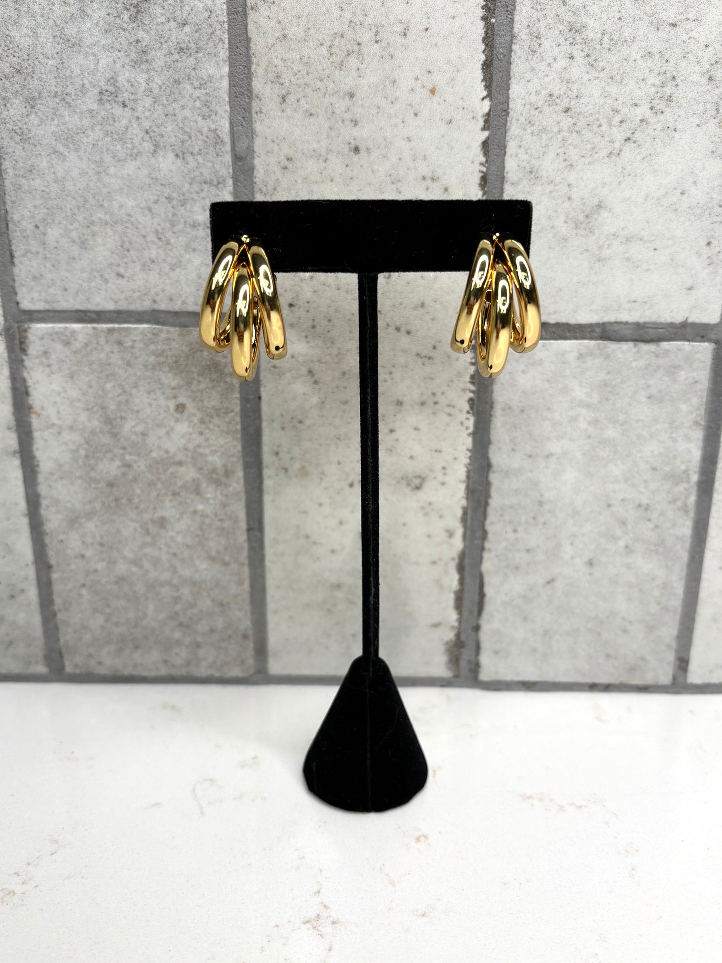 Gold triple hoop earrings on black display stand – trendy statement hoop earrings for women
