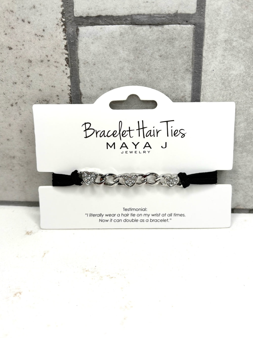Silver heart bracelet hair tie with rhinestone accents, black elastic hair tie bracelet, Maya J Jewelry accessory, crystal heart chain hair tie, stylish wrist hair tie for women, silver bracelet ponytail holder, chic everyday hair accessory