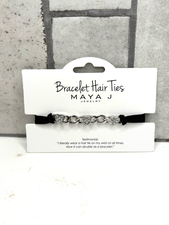 Silver heart bracelet hair tie with rhinestone accents, black elastic hair tie bracelet, Maya J Jewelry accessory, crystal heart chain hair tie, stylish wrist hair tie for women, silver bracelet ponytail holder, chic everyday hair accessory