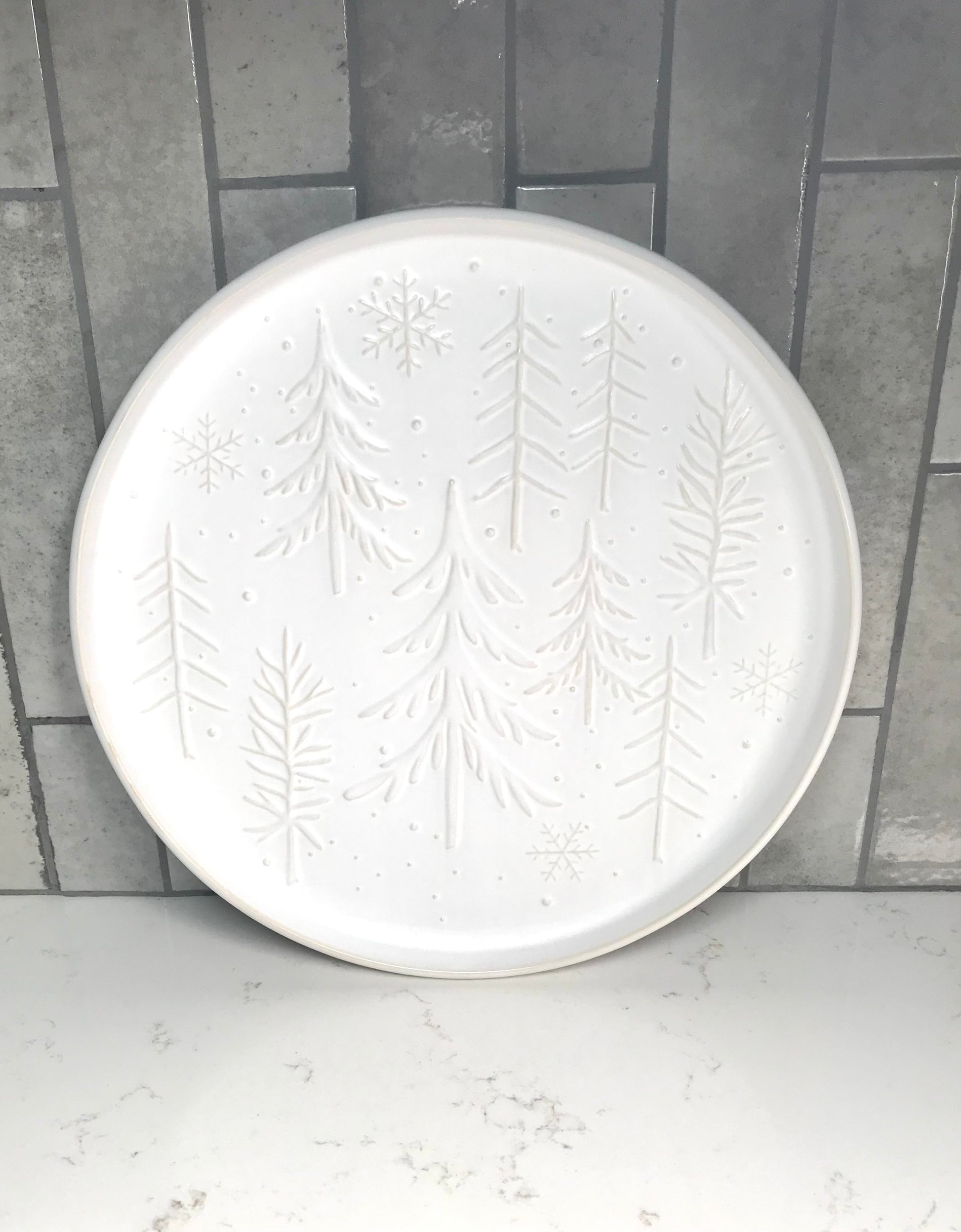 White ceramic plate with embossed tree design on a gray tiled background