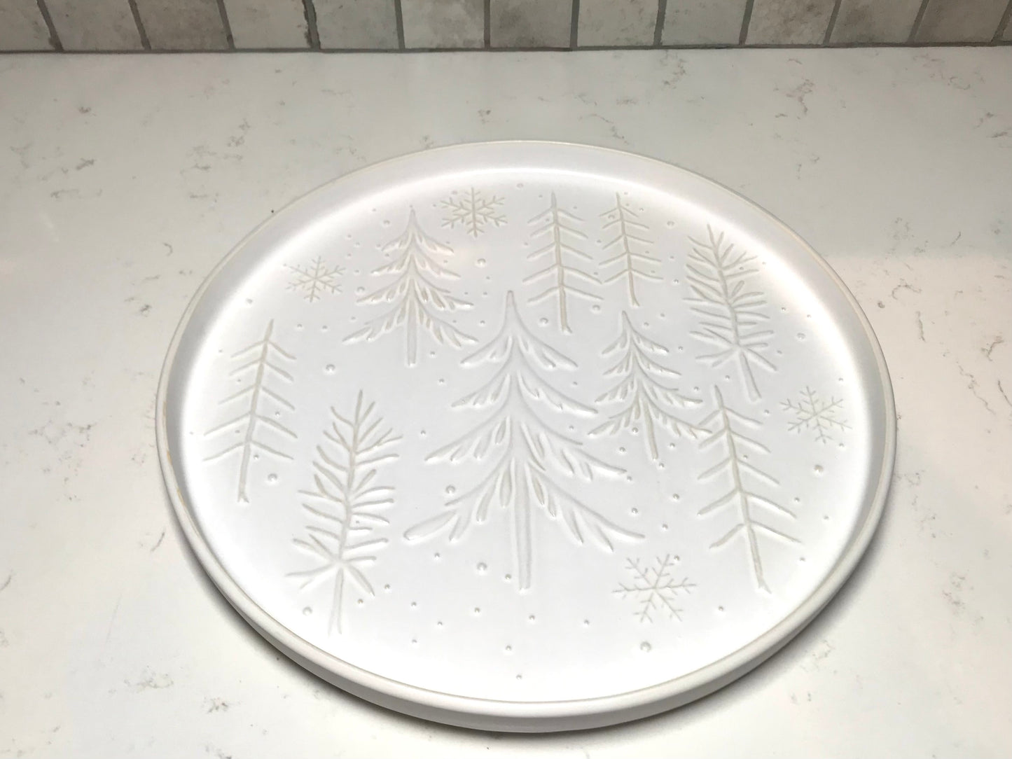 Round white plate with embossed tree design on a light gray surface