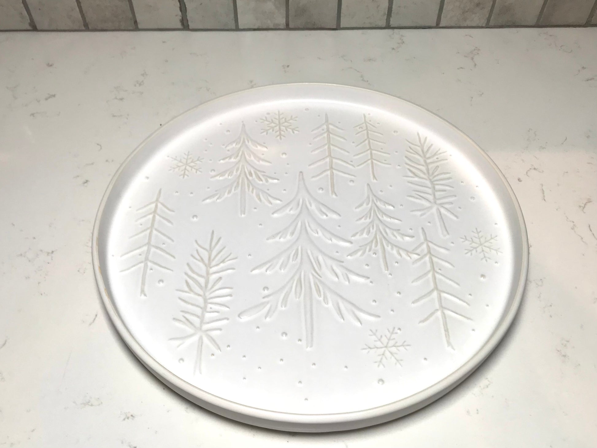 Round white plate with embossed tree design on a light gray surface