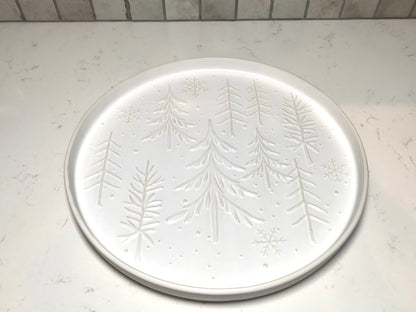 Round white plate with embossed tree design on a light gray surface