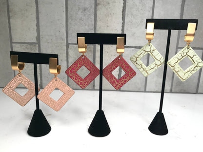Set of square-shaped earrings on black stands against a gray background