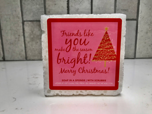 Soap in a sponge with a Christmas-themed label on a tiled bathroom floor.
