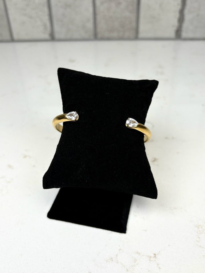 Gold open cuff bracelet with clear teardrop crystal accents displayed on a black velvet jewelry stand.