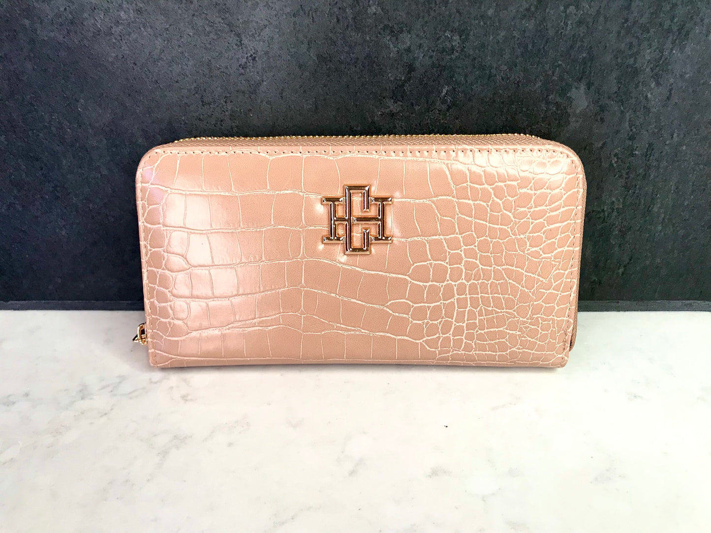 Tan crocodile-textured wallet with a gold Caroline Hill logo on a white surface and dark background