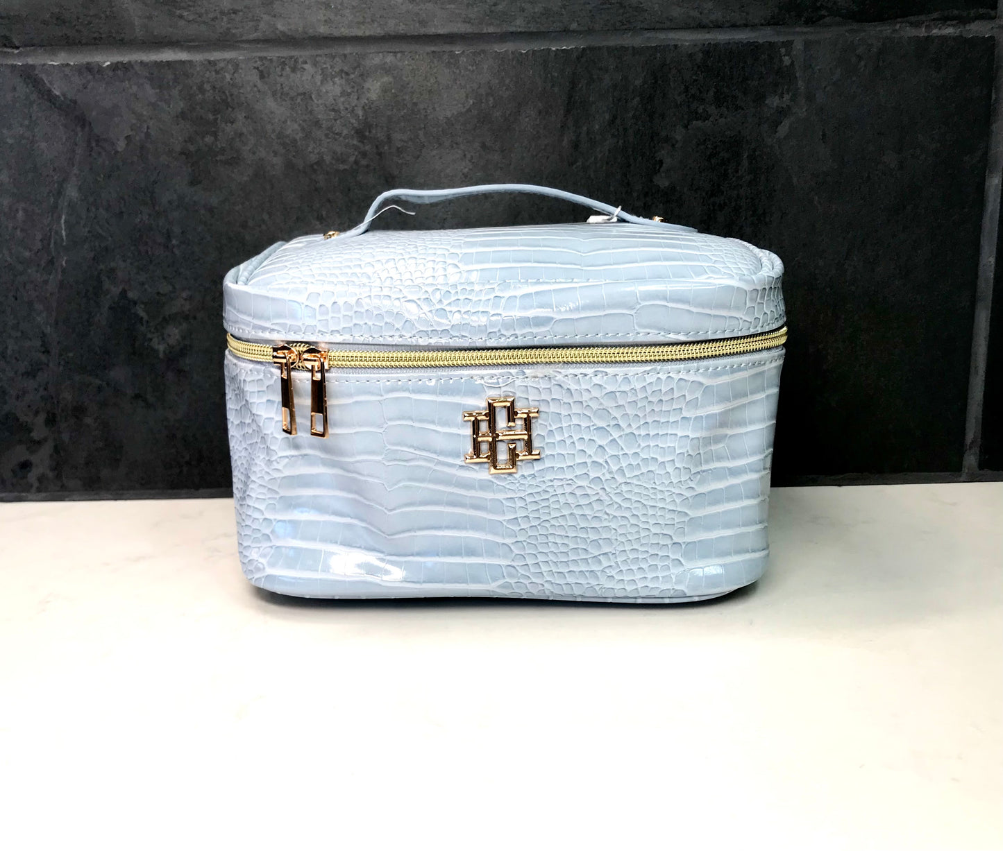 Light blue vanity bag with gold zipper and logo on a black background