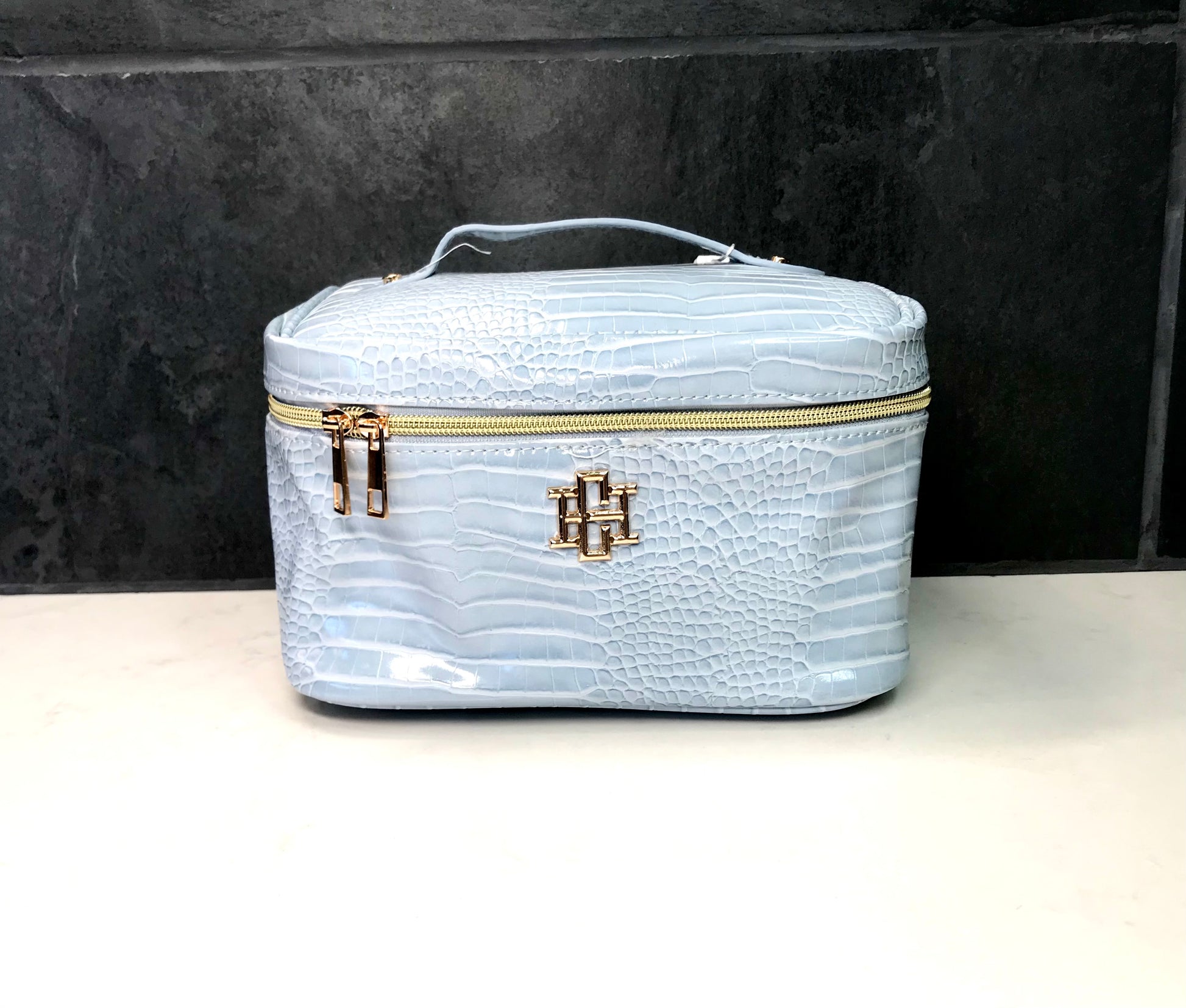 Light blue vanity bag with gold zipper and logo on a black background