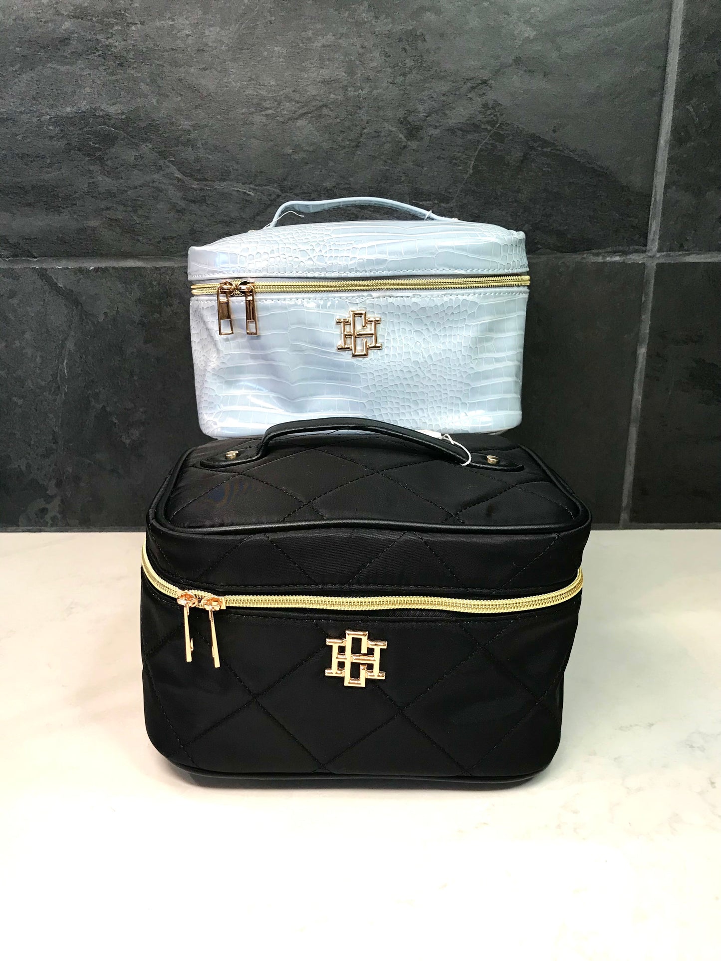 Black and white cosmetic bags with gold accents on a tiled wall background