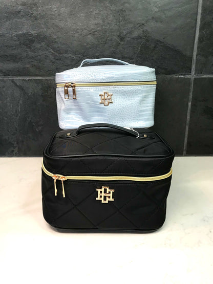 Black and white cosmetic bags with gold accents on a tiled wall background