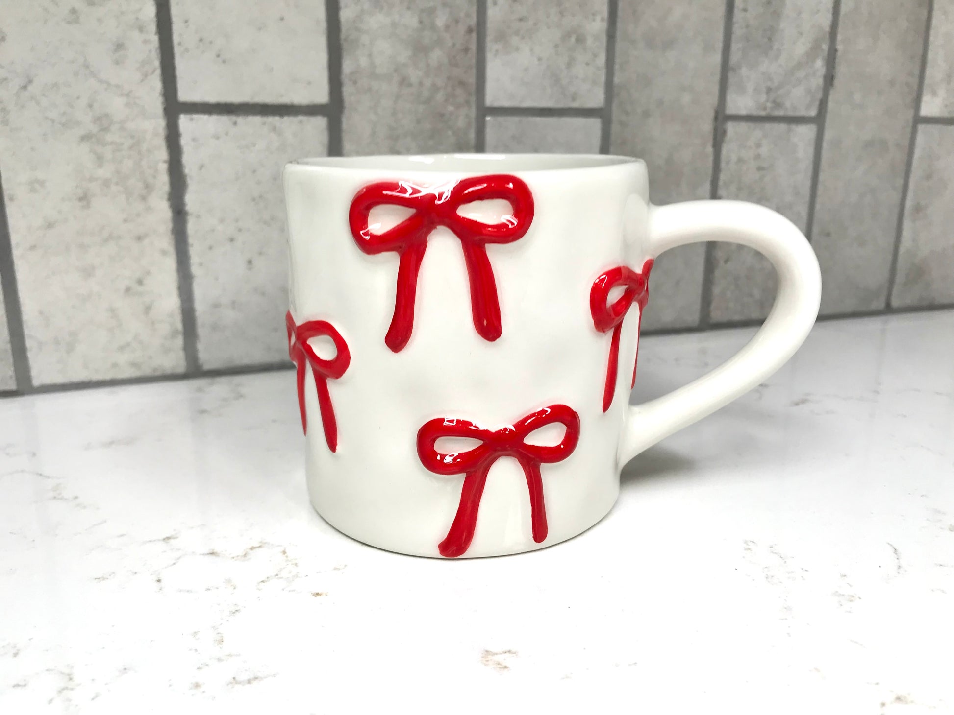 White mug with red bows on a white surface and gray tiled wall background