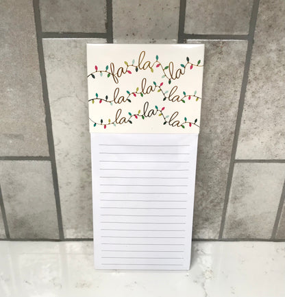 Notepad with 'fa la la la' text and Christmas lights design on a tiled floor background