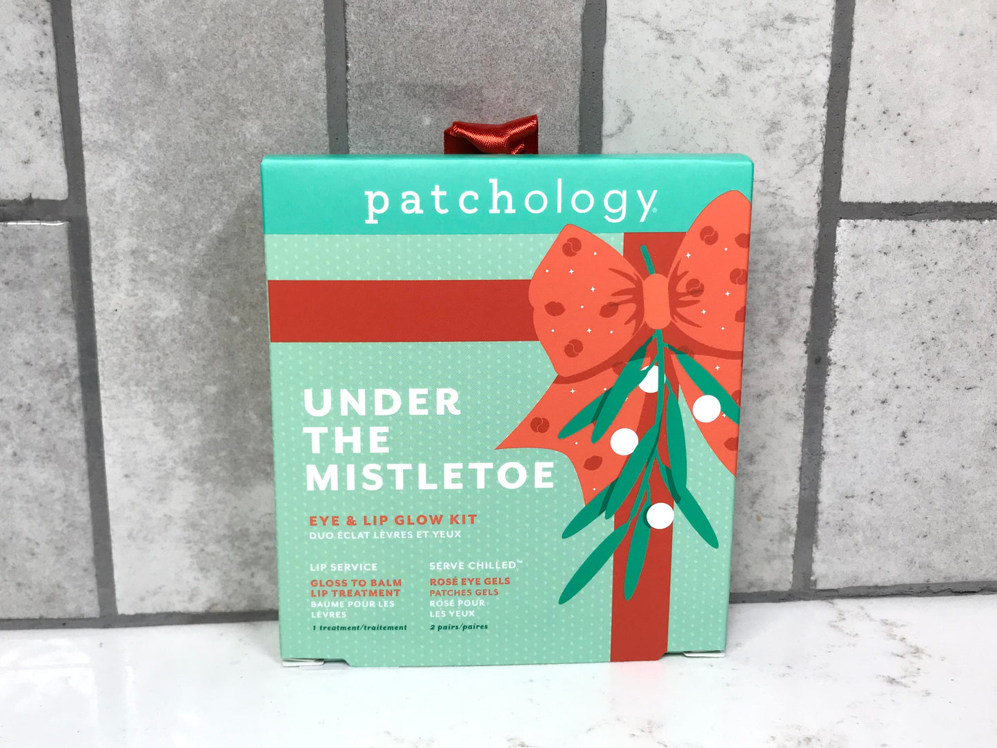 Patchology 'Under the Mistletoe' eye and lip glow kit on a textured surface with a gray background.