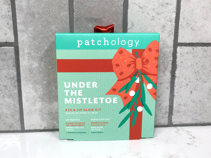 Patchology 'Under the Mistletoe' eye and lip glow kit on a textured surface with a gray background.