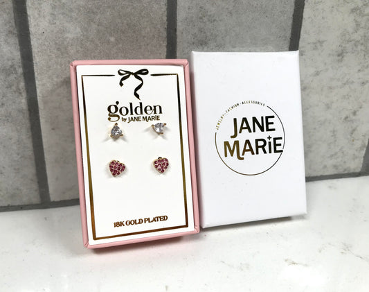 Kids 18K gold-plated earring set displayed in a pink Jane Marie gift box, featuring two pairs of studs: crystal bow studs on top and pink heart pavé studs on bottom. Box sits beside a white Jane Marie sleeve on a light tile background.