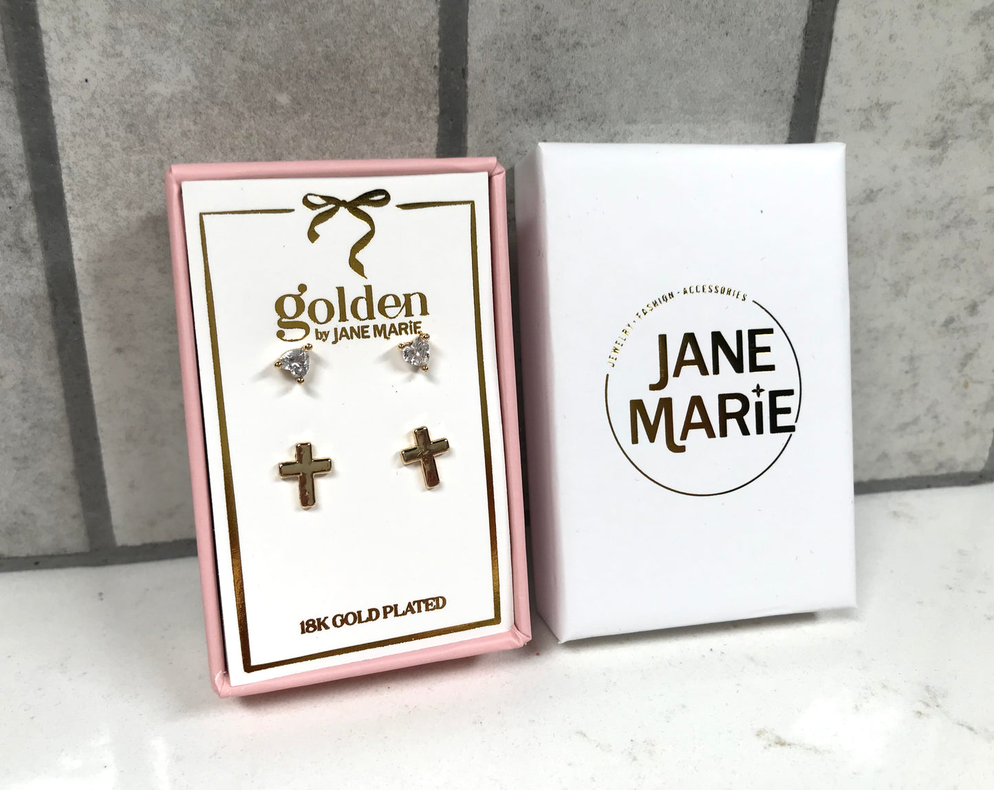 Kids 18K gold-plated stud earring set by Jane Marie, featuring crystal heart studs and small gold cross studs displayed in a pink gift box with white Jane Marie sleeve.